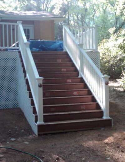 A deck with stairs leading to a house in the woods.