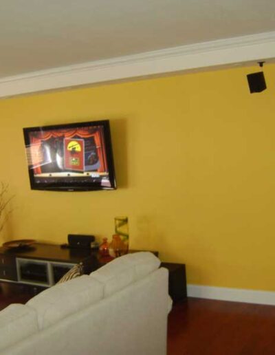 A living room with yellow walls and a tv on the wall.
